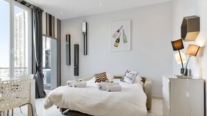 A modern hotel room with a large bed, a bedside table, a chair, a desk, and a balcony with a view.