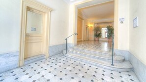 Un hall d’hôtel avec un sol en marbre, une porte en bois et un escalier menant à un autre espace.