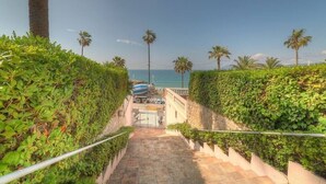 Un escalier menant à une plage bordée de palmiers, sous un ciel dégagé.