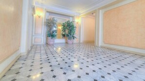 Un couloir doté d’un sol à carreaux, de plantes en pot et d’appliques murales.