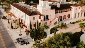 A large, pink building with a tower, surrounded by palm trees and a parking lot.