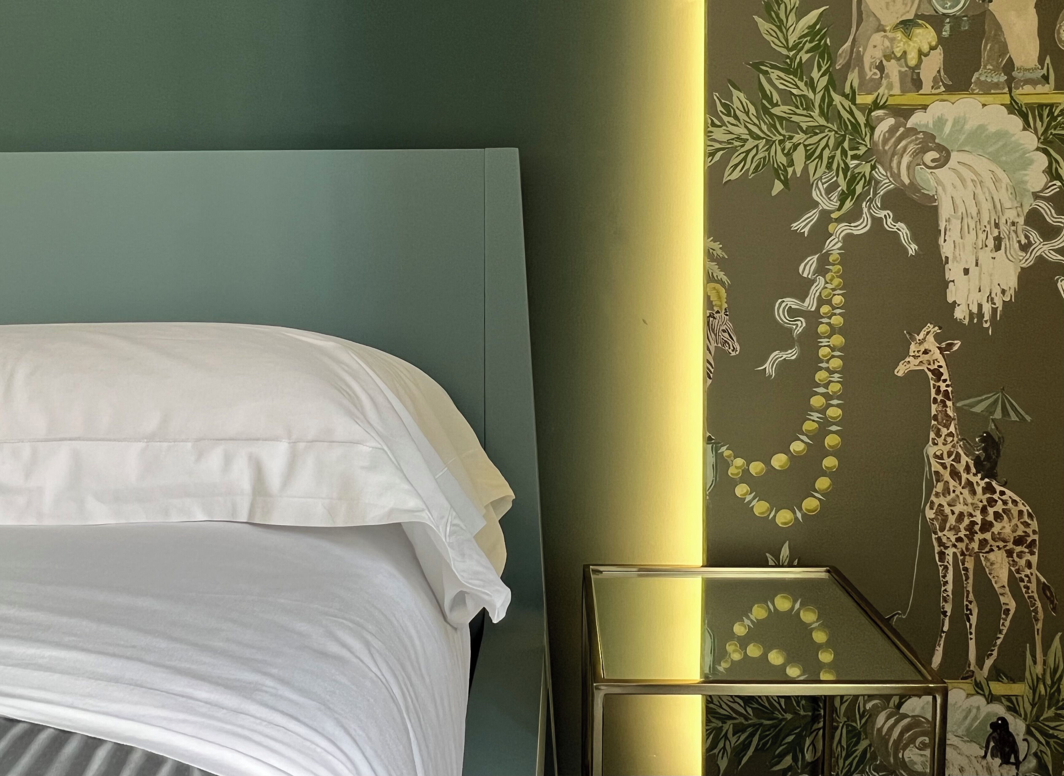 A bed with white linens, a nightstand with a lamp, and a wall with a nature-themed mural.