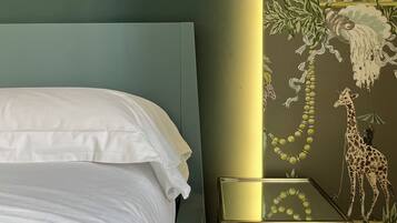 A bed with white linens, a nightstand with a lamp, and a wall with a nature-themed mural.