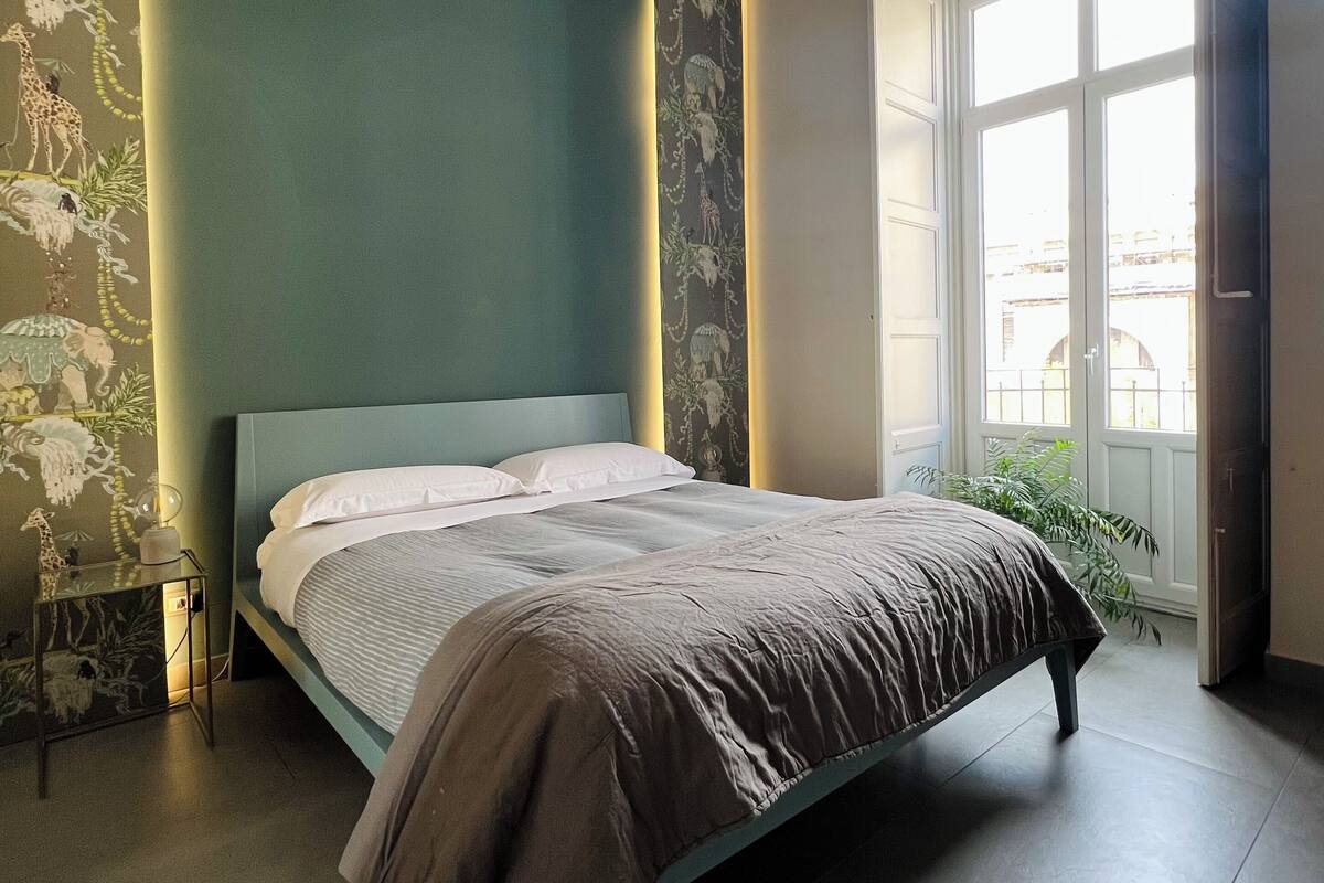 A bedroom with a bed, a bedside table, a window, and a door.