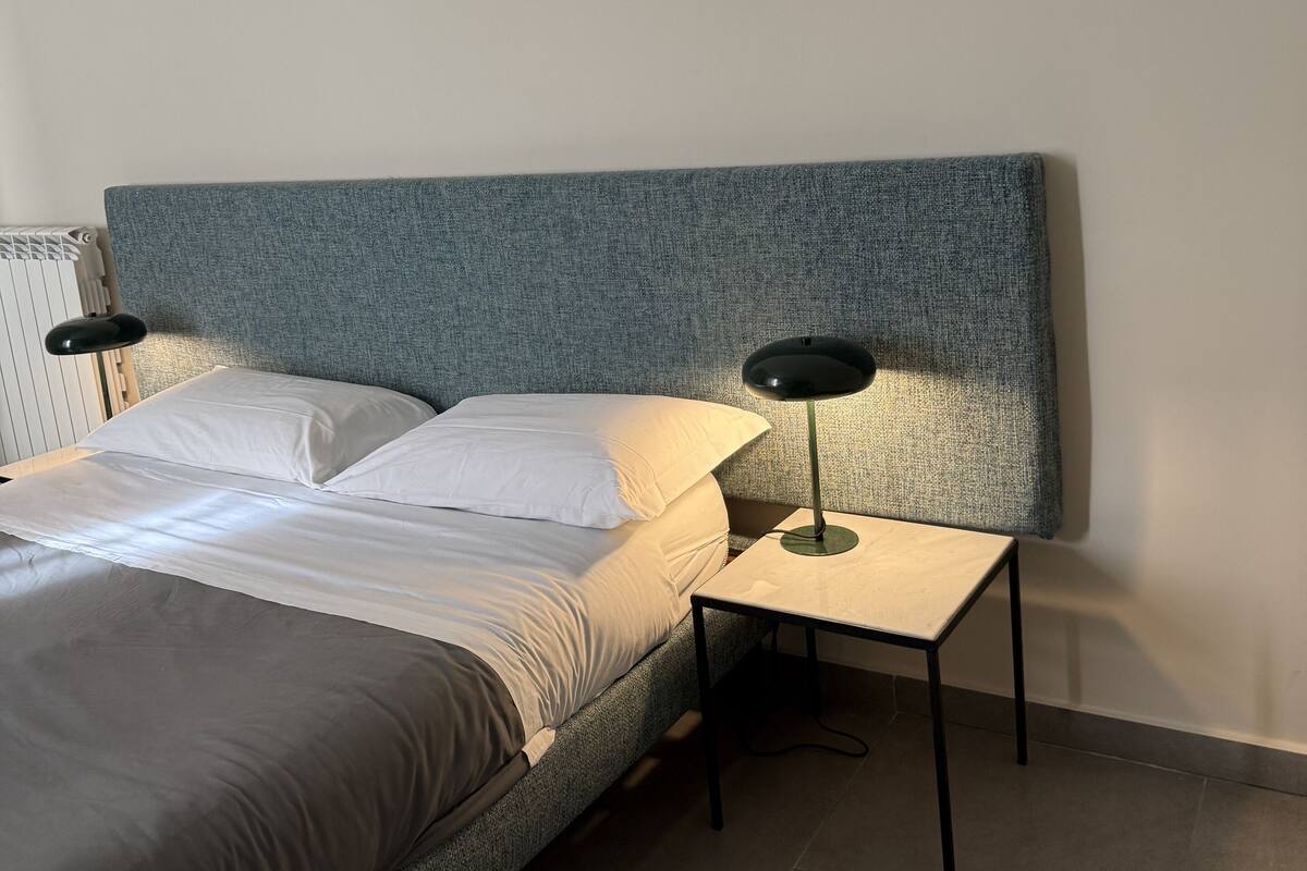 A neatly made bed with white linens, a grey headboard, and two bedside tables with lamps.