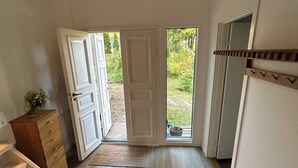 Una habitación con piso de madera, un banco, un aparador y una puerta que da al exterior.
