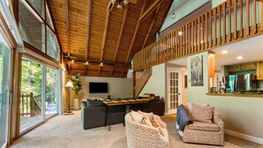 A spacious living area with a high ceiling, a staircase, a kitchen area, and a seating area with a sofa and armchairs. - 1 Min to Camelback! Creekside Escape + FirePit & BBQ (Tannersville)