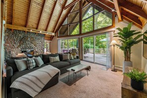 A cozy living room with a stone wall, a large window, and a wooden ceiling. - 1 Min to Camelback! Creekside Escape + FirePit & BBQ (Tannersville)