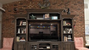A living room with a brick wall, a large flat-screen TV, and two patterned chairs. - Disney and Universal Studios only 30 minutes away (Eagle Lake)