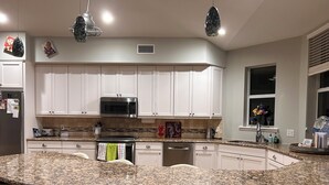 A modern kitchen with white cabinets, a granite island with bar stools, a built-in microwave, and a window with a flower vase. - Disney and Universal Studios only 30 minutes away (Eagle Lake)