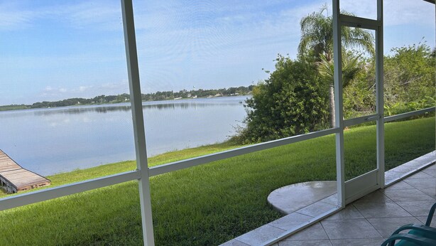 A view from a room with large windows overlooking a lake, a grassy area, and a tree. - Disney and Universal Studios only 30 minutes away (Eagle Lake)