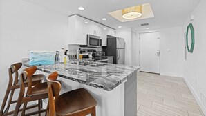 A modern kitchen with a marble island, stainless steel appliances, and wooden bar stools. - 2BR Bayview Condo with Balcony & Pool (Treasure Island)