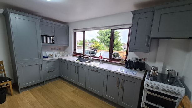 A kitchen with grey cabinets, a wooden floor, a window with a view of the outside, and a stove.