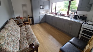 A compact kitchen with grey cabinets, a wooden floor, a sofa, and a dining table.
