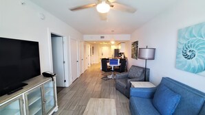 A living room with a television, sofa, and a ceiling fan. - Treasure Island Escape: 2BR Beach Views (Treasure Island)