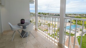 A balcony with a view of a beach and pool area, white chairs, and a small table with a plant. - Sophisticated Marina View 1BR Paradise (Río Hato)
