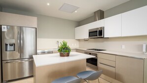 A modern kitchen with stainless steel appliances, a central island, and two bar stools. - Sophisticated Marina View 1BR Paradise (Río Hato)