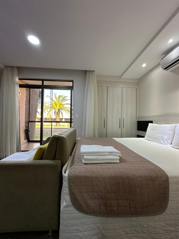 Une chambre d’hôtel avec un lit, un canapé, un bureau et une vue sur les palmiers par la fenêtre.