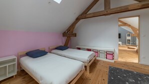 A bedroom with two beds, wooden beams, a skylight, and a view into another room.