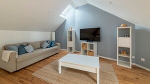 A modern living room with a sloped ceiling, a sofa, a coffee table, a TV, and built-in shelving.