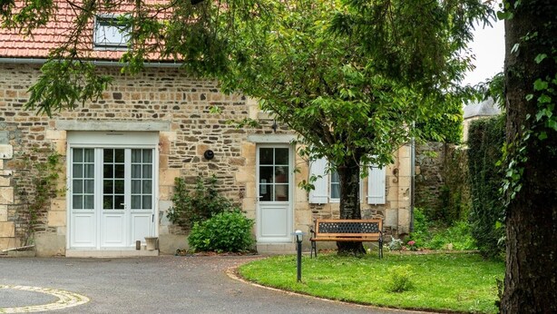 A stone building with a white door and windows, a bench, and a grassy area in front.