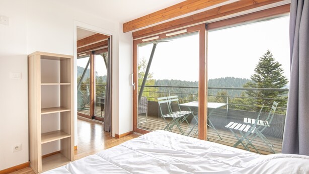 Ein Schlafzimmer mit einem großen Bett, einer Holzhilfe und einem Balkon mit Tisch und Stühlen.