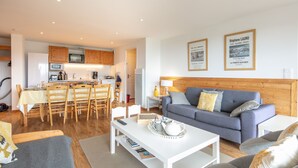 Ein modernes Wohnzimmer mit einem grauen Sofa, einem weißen Couchtisch und einem Essbereich mit Holzsesseln und einem Tisch.