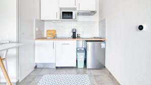 Eine kleine Küche mit weißen Schränken, einer Mikrowelle, einer Kaffeemaschine und einem kompakten Kühlschrank.