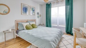 Ein modernes Schlafzimmer mit einem Bett, Nachttischen, einem Sessel und einem großen Fenster mit Vorhängen.