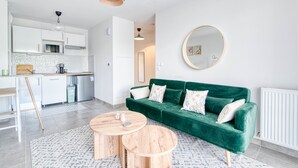 Ein modernes Wohnzimmer mit einem grünen Sofa, zwei Holztischen und einem runden Spiegel an der Wand.