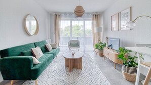 Ein modernes Wohnzimmer mit einem grünen Sofa, einem runden Couchtisch, einem Fernseher und einem großen Fenster mit Vorhängen.
