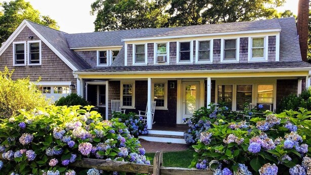 A two-story house with a front porch, surrounded by lush hydrangea bushes.