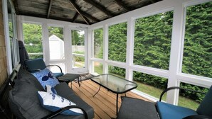 A covered porch with a wooden deck, a glass table, and two chairs.
