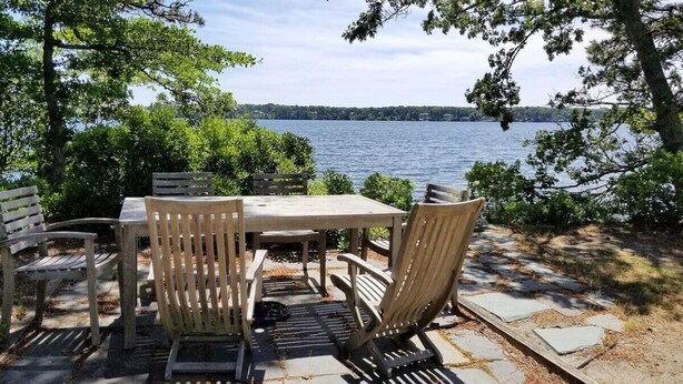 Un espace extérieur aménagé avec une table et des chaises, entouré d’arbres et offrant une vue sur un lac.