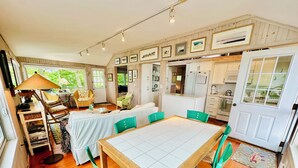 Un coin repas accueillant, avec une table en bois et des chaises vertes, entouré d’un parquet en bois et agrémenté de tableaux encadrés aux murs.