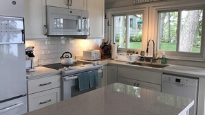 Une cuisine moderne avec des meubles blancs, un grand îlot central, un four à micro-ondes, un grille-pain et un lave-vaisselle.