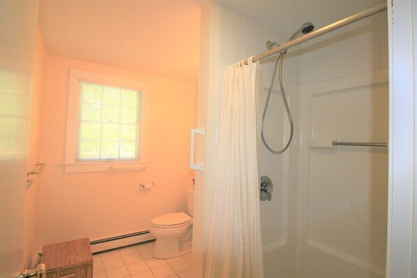 A bathroom with a toilet, a window, and a shower area.