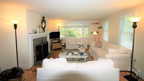 A living room with a fireplace, white sofas, a coffee table with books, and two floor lamps.