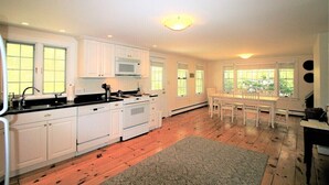 A kitchen with white cabinets, a stove, and a microwave. There is a dining table with chairs and a window with a view of greenery.