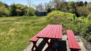 Et picnicbord i en græsplæne med et hus i baggrunden.