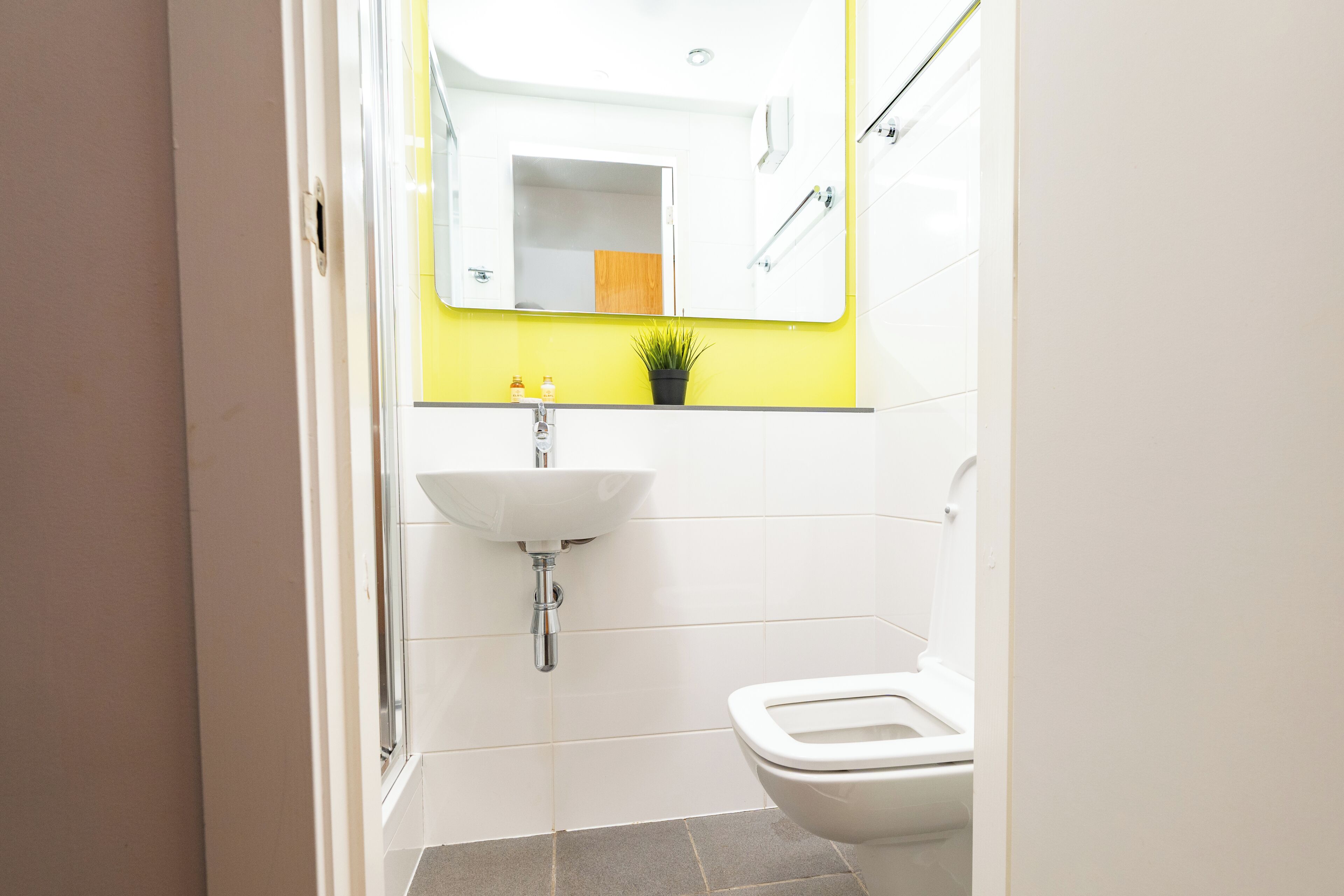 A bathroom with a white sink, a mirror, a toilet, and a yellow accent wall.
