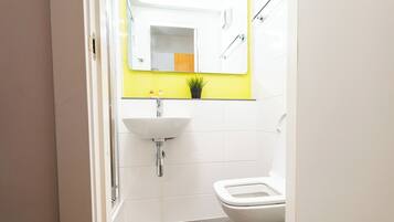 A bathroom with a white sink, a mirror, a toilet, and a yellow accent wall.