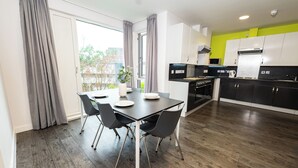 A modern kitchen with a dining area, featuring a dining table with chairs, a large window with curtains, and a view of the outside. - Binary Hub (Dublin)