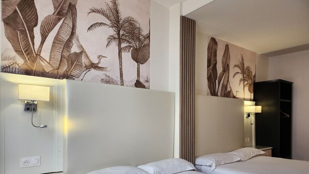 Ein Hotelzimmer mit zwei Betten, einem Nachttisch, einer Wandlampe und einem großen Spiegel.