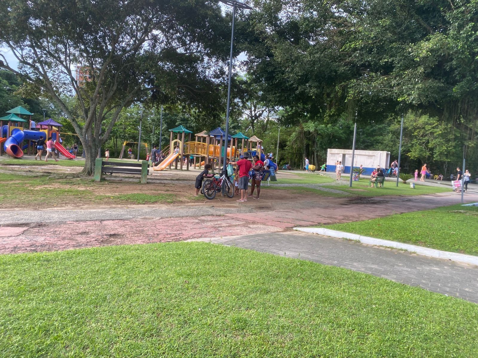Ein Spielplatz mit Rutschen und Klettergerüsten, umgeben von Bäumen und einem gepflasterten Weg.