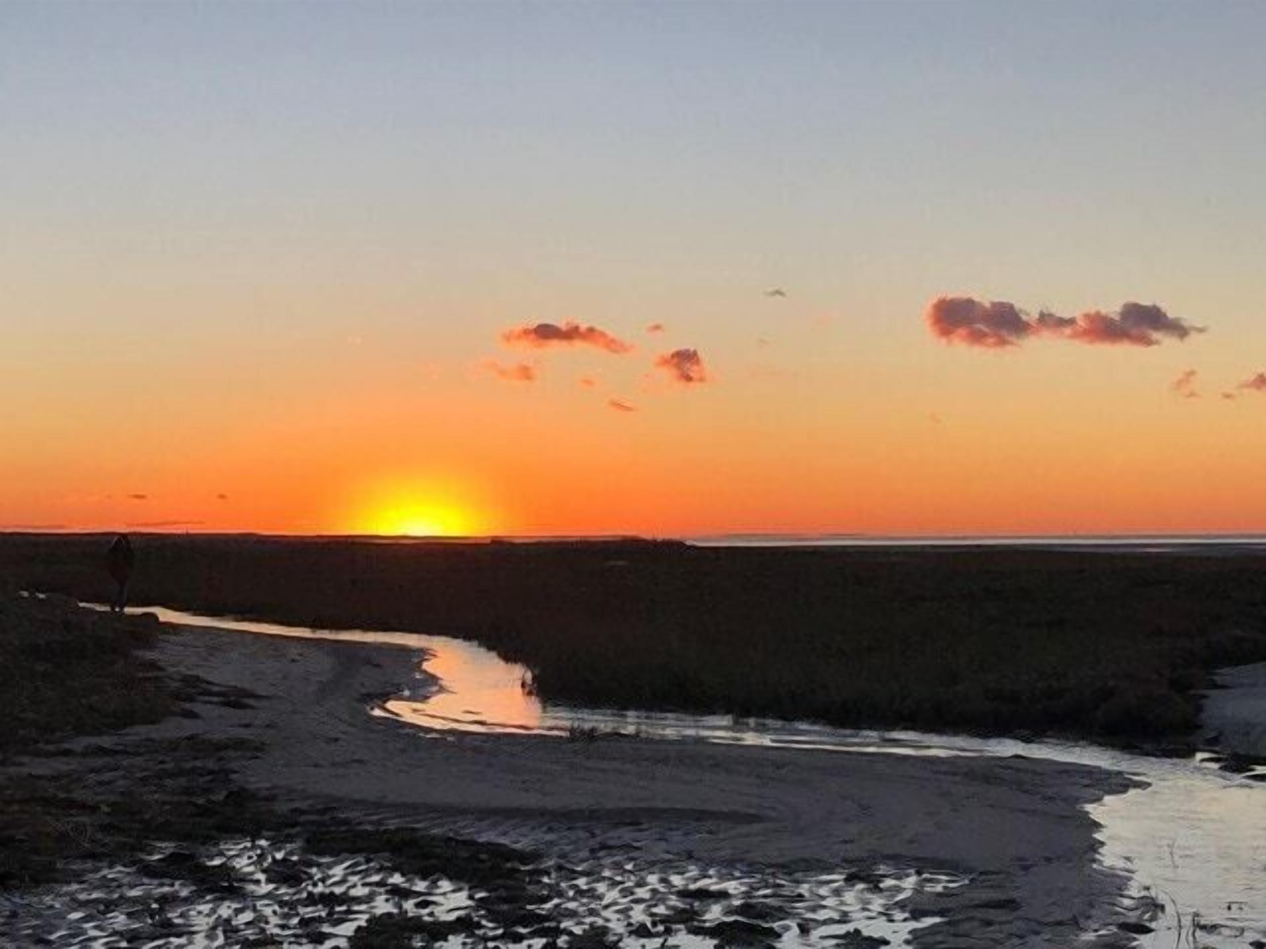 A sunset over a beach with a person walking along a path.