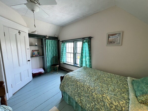 Une chambre à coucher avec un lit, une chaise, une étagère avec un miroir et une fenêtre avec des rideaux.