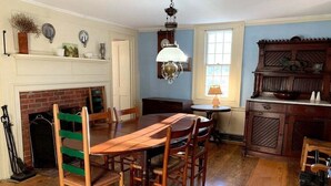 A dining room with a wooden table and chairs, a fireplace, a chandelier, and a wooden cabinet. - Discover the charm of HEWORL: Tonset Treasure, (Orleans)