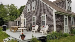 A two-story house with a covered patio area, a wooden deck, and outdoor furniture. - Discover the charm of HEWORL: Tonset Treasure, (Orleans)