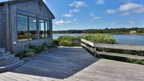 A wooden deck leading to a modern building with large windows overlooking a lake.